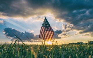 US Flag against sunset clouds background, grass in foreground