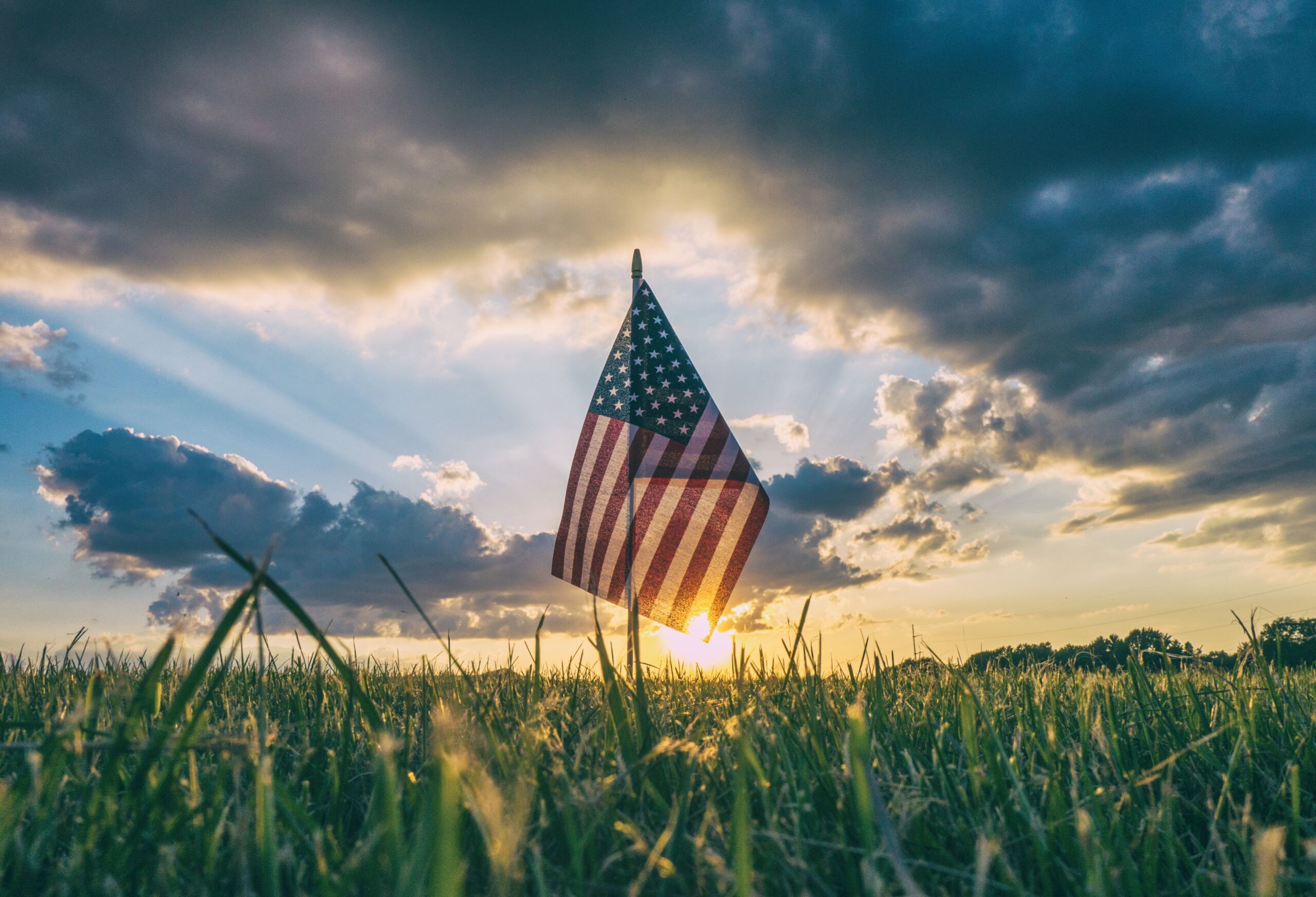 US Flag against sunset clouds background, grass in foreground